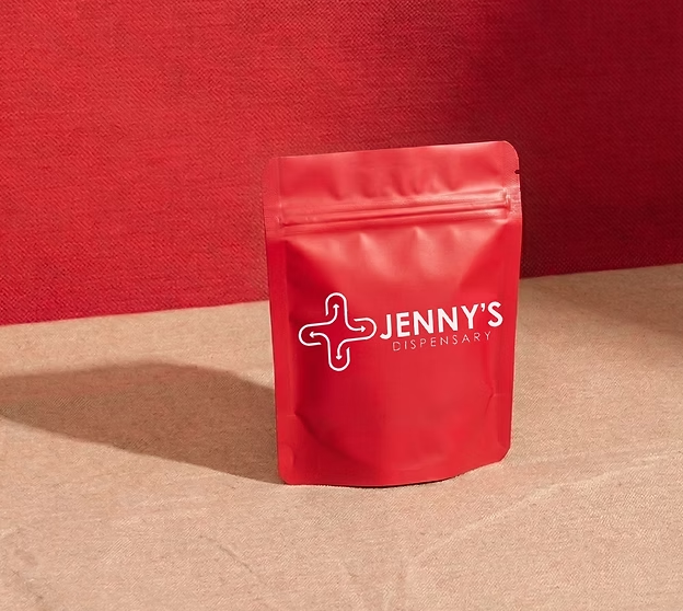 A red Jenny's Dispensary mylar bag standing on a pink floor
